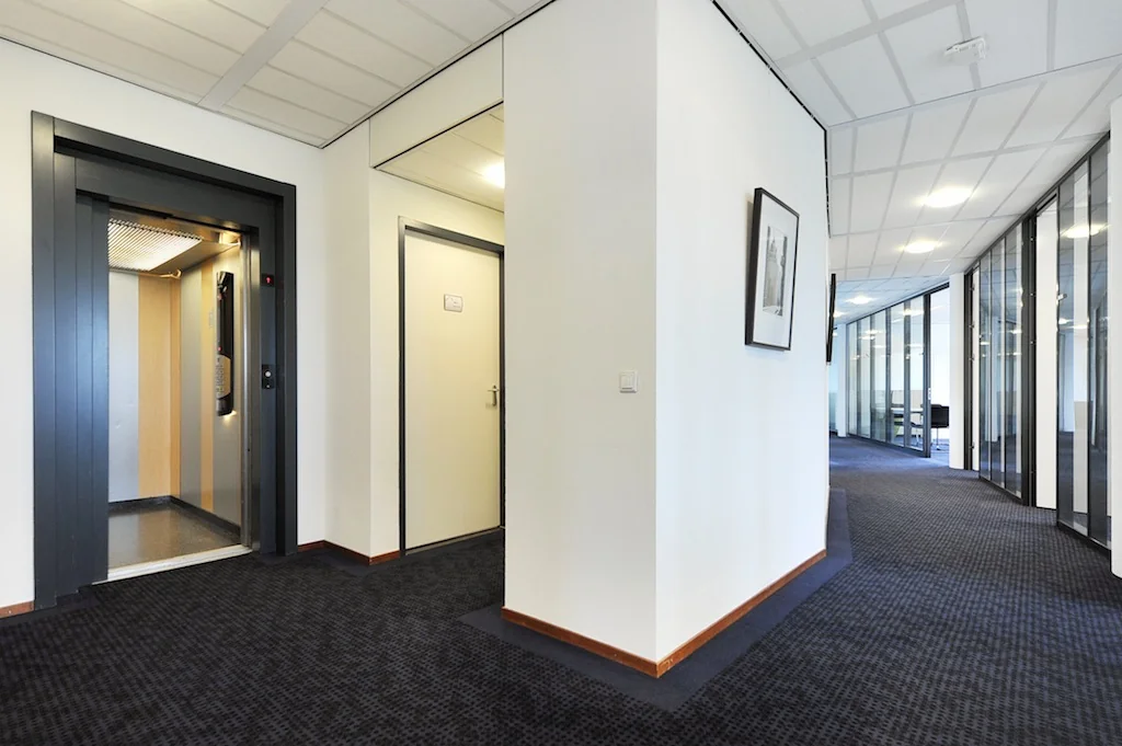 Moderne kantoorgang aan de Laan van S‐Gravenmade met lift, deuren en glazen kantoorwanden.